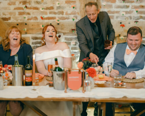 Bride, groom and family at the top table of a Worcestershire barn wedding laughing at Brett Sirrell's magic