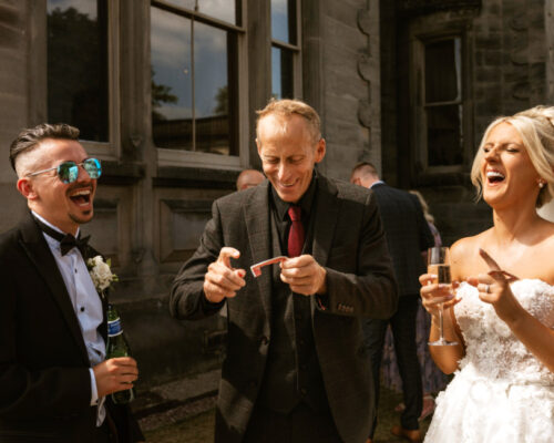 FirewoodFilmPhotography Bride and Groom bursting out in laughter as they see a bespoke magic trick for just them, during the drinks reception at a manor wedding venue