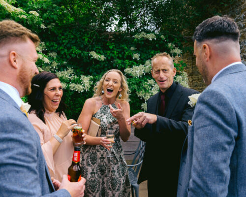 Luke hardy dodford manor during the drinks reception at a Cotwolds wedding, a group of friends share a joke and laugh with the magic